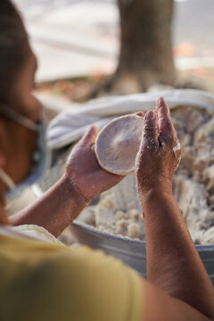 Unrecognizable elderly woman preparing corn tortillas by hand on a griddle in her modest street kitchen