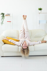 Smiling blonde woman sitting on comfortable coach in living room in pajama - homewear and free time holidays at home concept