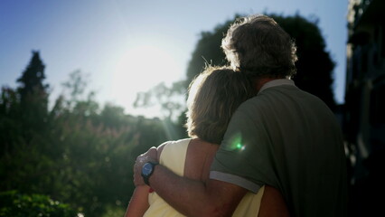Romantic senior couple looking at sunset together. Senior husband with arm around wife standing outdoors at park