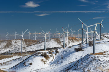 Wind turbines on a windmill farm for alternative energy production shown in the snow-covered...
