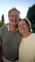 Portrait of a senior couple posing for camera standing outdoors in sunlight with flare. Close up older married husband and wife faces smiling outside in Vertical Video