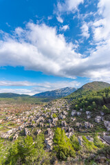 Fototapeta na wymiar View of Kayakoy Fethiye with abandoned buildings and clouds on blue sky and green grass