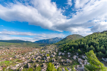 View of Kayakoy Fethiye with abandoned buildings and clouds on blue sky and green grass