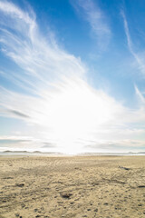 Fototapeta na wymiar Dazzling rays from a cloudy blue sky on a sandy beach