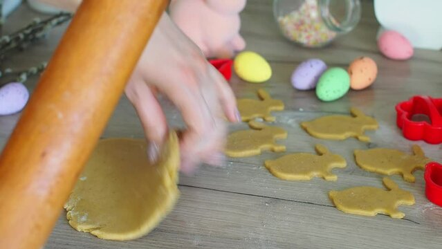 Womens hands close-up kneading ginger dough and carving figurines from it. The shapes of rabbit. Cutting sugar cookie dough with Easter shaped cookie cutters. Preparation for Easter. Holidays baking.