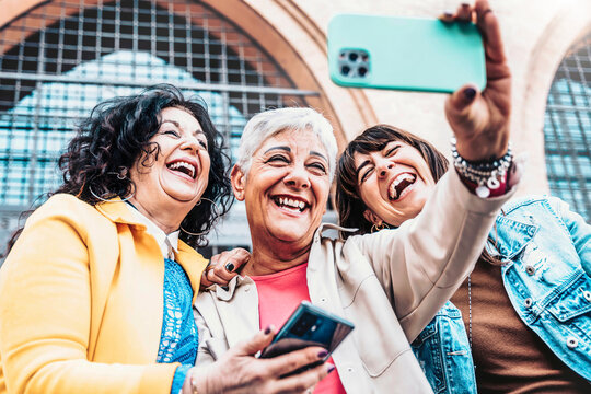 Three cheerful women chilling outside taking group selfie and smiling - Happy female senior friends enjoying the weekend together while sightseeing an italian city - Elderly people lifestyle concept.