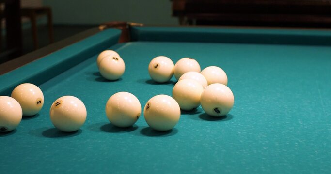 The hands of a man lay out white billiard balls on a green table. The beginning of the game in Russian billiards. White balls lie scattered on the green surface of the billiard table.