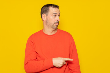 Bearded hispanic man wearing a red sweater pointing to the side with the index finger isolated on yellow studio background