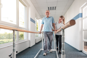 Senior Patient and physical therapist in rehabilitation walking exercises, she is helping him along the bars - 580848898