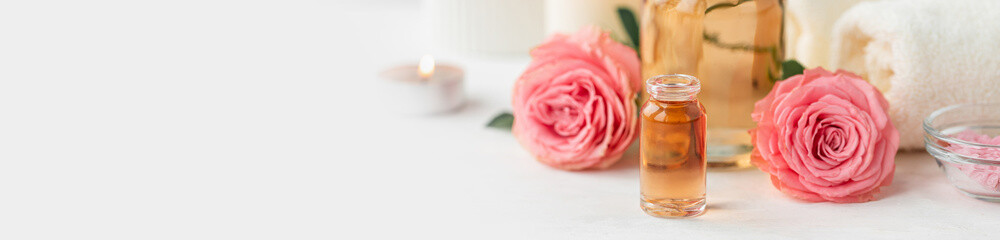 Aromatherapy. Pure organic essential rose oil concept. Elixir with plant based floral herbal ingredients. Pink flowers extract. Spa atmosphere with candle, towel. White background. Banner copy space