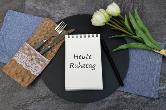 Heute Ruhetag auf einen Notitzblock geschrieben mit Besteck, Blumenstrau&szlig; und einem Stift.