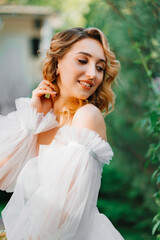 a bride in an open-shouldered dress poses against the backdrop of greenery
