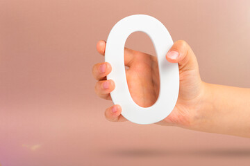 Numeral zero in hand. A hand holds a white number zero on a red background with copy space. Zero...