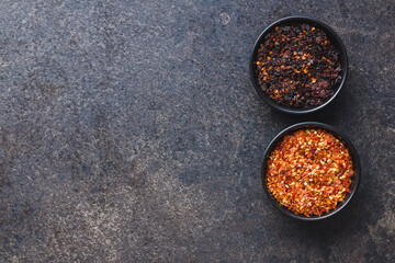 Smoked dry chili pepper flakes. Crushed red peppers in bowl on black table.