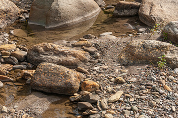 Denali Park, Alaska, USA - July 24, 2011: Nenana River. Closeup of still water puddles among gray-brown pebbles and boulders