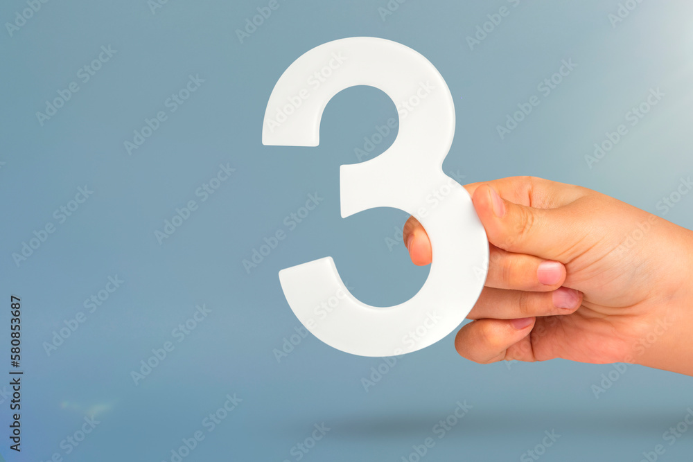 Aufkleber number three in hand. hand holding white number 3 on blue background with copy space. concept with n