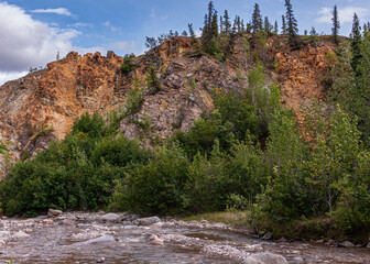 Denali Park, Alaska, USA - July 24, 2011: Nenana River. Fast running water and rocky shoreline, green tree foliage with red rock flanks under blue sky