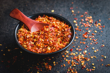 Dry chili pepper flakes. Crushed red peppers in bowl on black table.