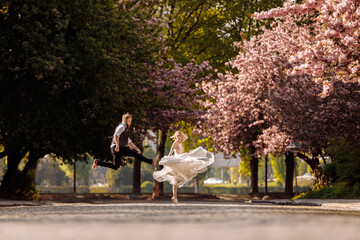 Obraz premium Beautiful, cheerful and lively newlyweds, groom and bride are hugging near the blooming pink cherry blossom. Wedding portrait of a close-up of a smiling bearded groom and a cute bride.