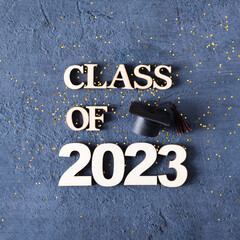 Class of 2023 concept. Wooden number 2023 with graduated cap on dark concrete background with tinsel