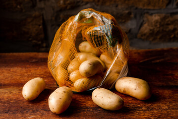 Potatoes in package on wooden background. Buying or selling potatoes in polyethylene mesh. Dark background.