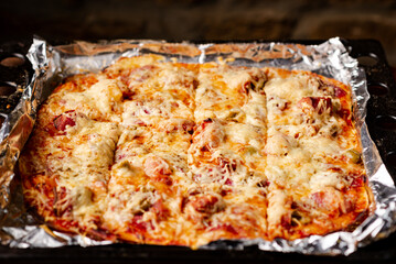 Cooked homemade pizza on baking sheet. Pizza with cheese, tomatoes, ham on baking sheet.