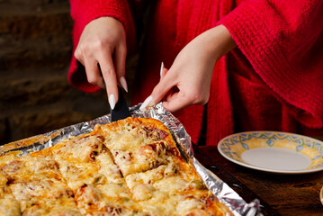 Unrecognizable girl takes piece of homemade pizza. Woman's hand with long nails holds kitchen spatula.
