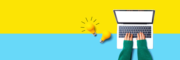 Person using a laptop computer and light bulbs - Flat lay