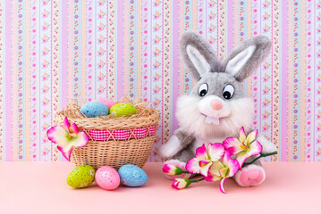 Decorative Easter bunny and colored eggs in a basket. Easter decor. Happy Easter. Pink background shabby chic.