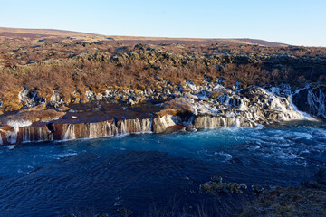 magnifique cascade gelé avec une eau sortant directement de la roche avec eau de rivière turquoise sur une montagne ensoleillé d'Islande - obrazy, fototapety, plakaty