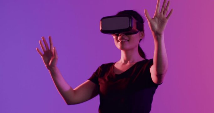 Happy asian woman using vr headset and touching virtual screen on purple background, slow motion