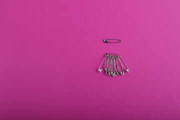 An example of a beautiful safety pin in silver, below is a large bunch of safety pins in various sizes and shapes, against a bright pink textured background. Sewing accessories. Copy space view