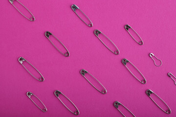 A pattern of metal safety pins of various sizes and shapes, which are laid out in straight lines on a hot pink textured background. Sewing accessories