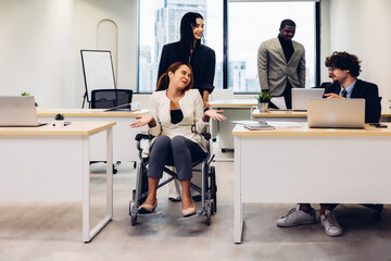 Group of corporate colleagues work together at office. Office workers and woman on a wheelchair in bright office. They are showing a teamwork. 