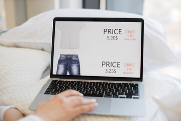 Close up of woman using wireless laptop for browsing shopping site during sale. Caucasian female ordering white t-shirt and blue jeans online while staying at home.