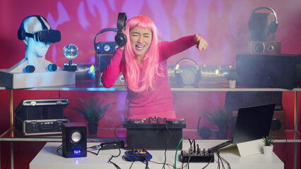Asian performer mixing stereo sounds with electronics, standing at dj table performing remix using professional mixer console. Cheerful artist enjoying playing music in nightxlub, having fun with fans