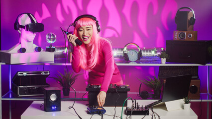 Asian musician standing at dj table playing techno music using professional mixer console, enjoying to perform at night in club. Cheerful performer having fun with fans during techno concert