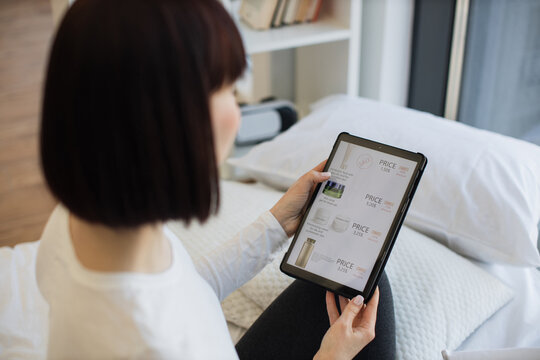 View Over Shoulder Of Beautiful Woman Resting On Bed At Home And Using Digital Tablet For Searching Cosmetic With Discount Online. Concept Of People, Modern Gadgets And Consumerism.