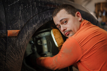 Mechanic man repairs the undercarriage of the car. A man repairs a car in a garage. Car wheel repair