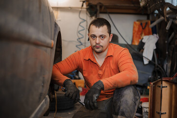 Mechanic man repairs the undercarriage of the car. A man repairs a car in a garage. Car wheel repair