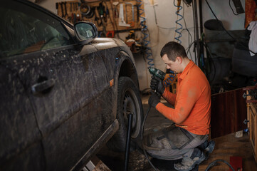 Fototapeta na wymiar Mechanic man repairs the undercarriage of the car. A man repairs a car in a garage. Car wheel repair