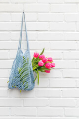 Pink tulips in a mesh bag against a white brick wall