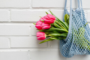 Close-up of pink tulips bouquet in a mesh bag against a white brick wall