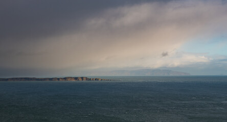 Vast seascape with island illuminated through a break in storm clouds - Northern Ireland