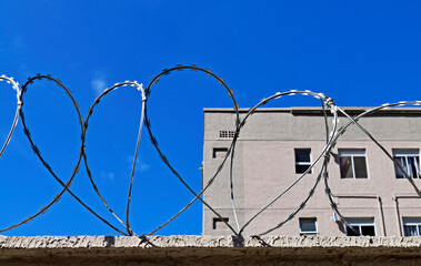 Barbed wire on top of the wall and grey buikding in the background
