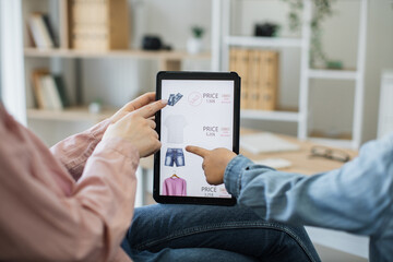Close up of digital tablet with commercial newcommers of clothes available at discount on screen. Mother and child hanging out in apartment and enjoying internet shopping via electronic gadget.