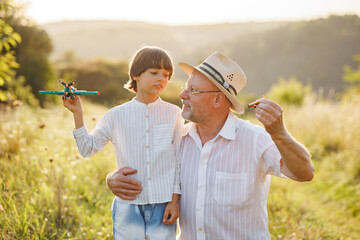 Little boy with his grandfather standing in a field with a two toys plane at summer