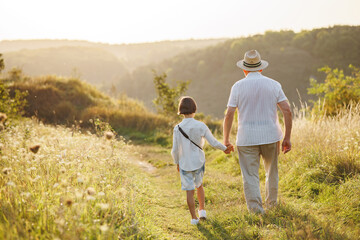 Backside photo of a little boy with his grandfather walking in a field at summer