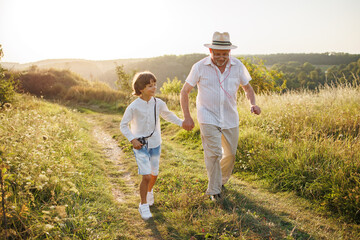 Photo of a little boy with his grandfather walking in a field at summer