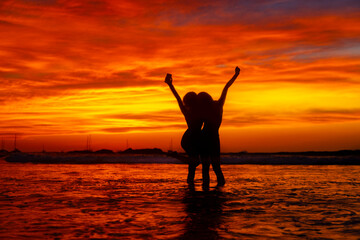 Sunset silhouette of two friends with arms raised